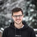 A man with glasses wearing a black hoodie, looking directly at the camera.