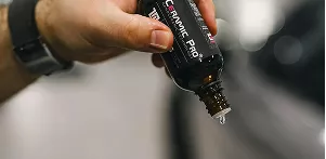 A person holding a bottle of car wax, preparing to apply it to a vehicle's surface for shine and protection