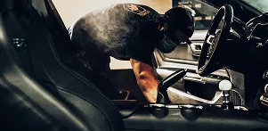 A man is vacuuming and cleaning the interior of a car, focusing on the seats and dashboard