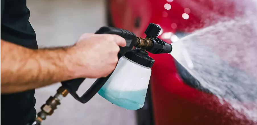 A person cleaning a car with a spray gun, focusing on removing dirt and grime from the vehicle's surface