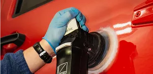 A person wearing blue gloves operates a car wash machine, cleaning a vehicle with water and soap