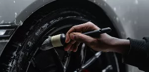 A person brushes dirt off a car tire, focusing on cleaning and maintaining the vehicle's appearance