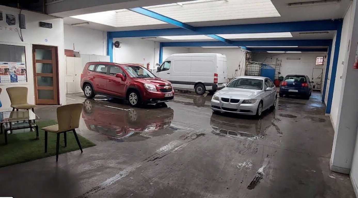 Two men washing a black BMW SUV at a car wash, surrounded by soap and water spray